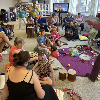 Vista's community room is filled with families taking part in a music workshop. There are tambourines, drums and maracas being used.