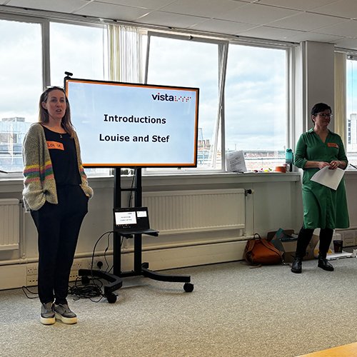 Louise Vista’s CEO and Stef our Reset Strategy day facilitator stand next to a large presentation screen with 'Introduction. Louise and Stef' on the screen. There is a long panel of windows behind them.